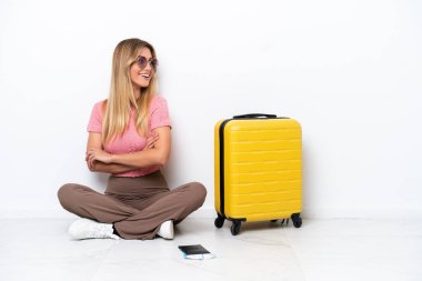 Uruguaylı gezgin kadın, beyaz arka planda, kolları bağlı ve mutlu bir şekilde yerde oturuyor.