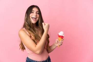 Pembe arka planda izole edilmiş kornet dondurmalı beyaz bir kadın zaferi kutluyor.