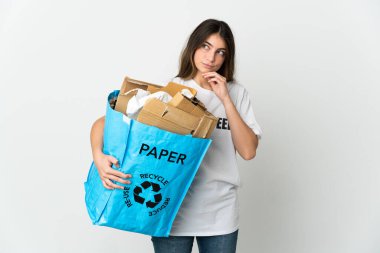 Elinde kağıt dolu bir geri dönüşüm çantası tutan genç bir kadın beyaz arka planda izole edilmiş ve yukarı bakıyor.