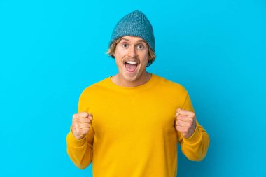 Yakışıklı sarışın adam mavi arka planda tek başına zaferi kutluyor.