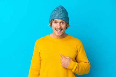 Yakışıklı sarışın adam, mavi arka planda mahsur kalmış, şaşırmış bir yüz ifadesi var.