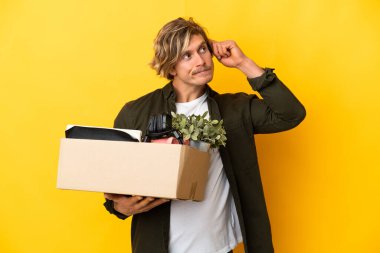 Sarışın adam sarı arka planda izole edilmiş şeylerle dolu bir kutuyu kaldırırken hareket ediyor. Şüpheleri ve düşünceleri var.