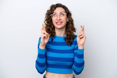 Beyaz arka planda izole edilmiş beyaz tenli genç bir kadın parmaklarını çapraz yapıp en iyisini diliyor.