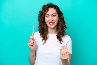 Mavi arka planda dişlerini fırçalayan beyaz genç bir kadın, elini uzatmaya davet ediyor. Gelmene sevindim.