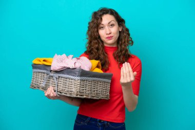 Elinde çamaşır sepeti olan beyaz bir kadın mavi arka planda izole edilmiş bir şekilde el ele gelmeye davet ediyor. Gelmene sevindim.