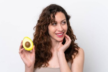 Beyaz arka planda izole edilmiş beyaz bir kadın elinde bir avokado tutarken gülümsüyor. Portreyi kapat