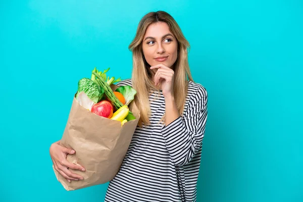 Young Uruguayan Woman Holding Grocery Shopping Bag Isolated Blue Background — стоковое фото