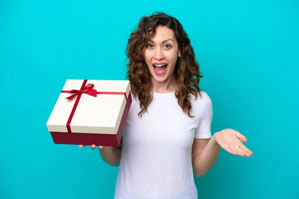 Young Caucasian Woman Holding Gift Isolated Blue Background Shocked Facial — 스톡 사진