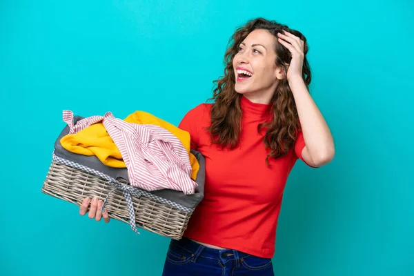 Mavi arka planda izole edilmiş çamaşır sepetini tutan beyaz bir kadın.