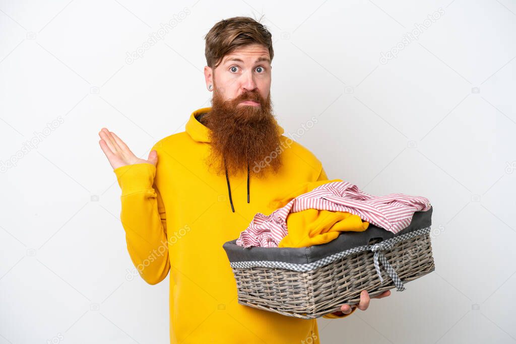 Redhead man with beard holding a clothes basket isolated on white background having doubts while raising hands