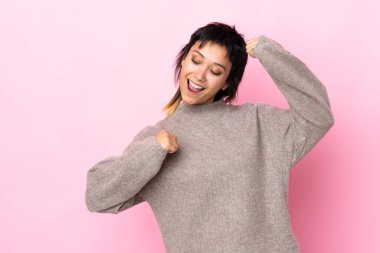 Genç Uruguaylı kadın izole pembe arka planda zaferi kutluyor.