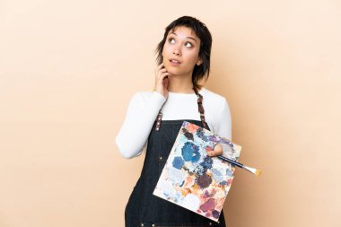 Genç bir sanatçı arka planda bir palet tutarak bir fikir düşünüyor.