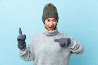 Kışlık şapkalı genç Uruguaylı kız mavi arka planda mahsur kalmış ve yüzünde sürpriz bir ifade var.