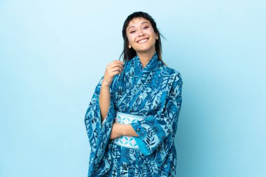Kimono giyen genç bir kadın mavi arka planda gülüyor.