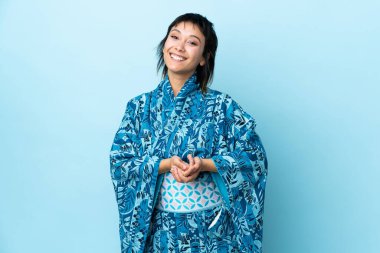 Kimono giyen genç bir kadın mavi arka planda gülüyor.