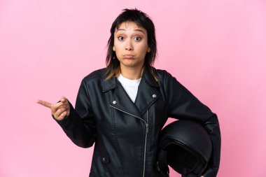 Genç Uruguaylı bir kadın pembe arka planda motosiklet kaskı tutuyor.