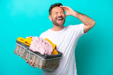 Mavi arka planda izole edilmiş çamaşır sepetini tutan orta yaşlı kadın çok gülümsüyor.