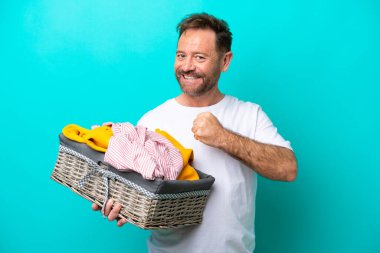 Mavi arka planda izole edilmiş çamaşır sepetini tutan orta yaşlı bir kadın zaferi kutluyor.