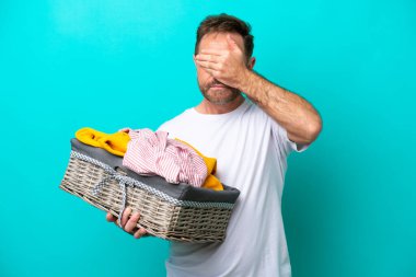 Orta yaşlı bir kadın, mavi arka planda elleri kapalı bir çamaşır sepetini tutuyor. Bir şey görmek istemiyorum.