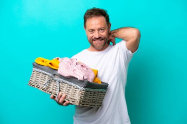 Mavi arka planda izole edilmiş çamaşır sepetini tutan orta yaşlı kadın gülüyor.