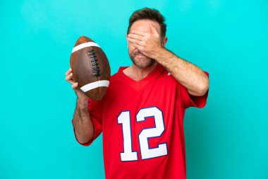 Orta yaşlı, ragbi oynayan beyaz bir adam mavi arka planda tek başına gözlerini elleriyle kapatıyor. Bir şey görmek istemiyorum.