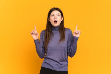 Sarı arka planda izole edilmiş genç Ukraynalı kız şaşırmış ve işaret ediyor.