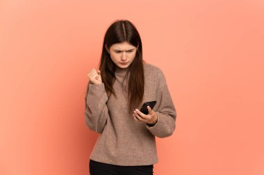 Pembe arka planda izole edilmiş genç Ukraynalı kız parmakları çapraz cep telefonu kullanıyor.