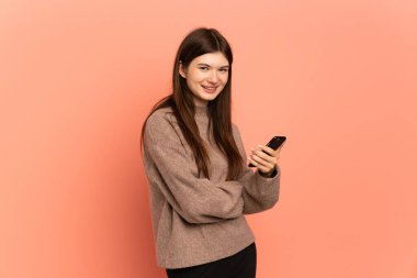 Pembe arka planda izole edilmiş genç Ukraynalı bir kız cep telefonu tutuyor ve kollarını kavuşturuyor.