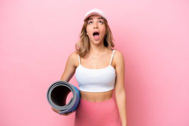 Genç sporcu kadın, elinde minderle yoga derslerine gidiyor. Şaşkın şaşkın bakıyor.