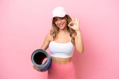 Genç sporcu kadın yoga derslerine giderken elinde paspas tutarken tamam işaretini parmaklarıyla gösteriyor.