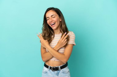 İzole edilmiş mavi arka planda genç bir kadın gülümsüyor ve zafer işareti gösteriyor