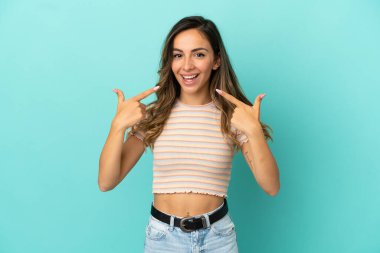 Soyutlanmış mavi arka planda genç bir kadın baş parmak işareti yapıyor.
