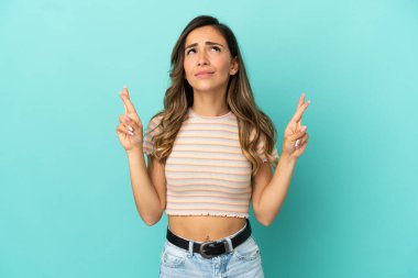 İzole edilmiş mavi arka planı olan genç bir kadın parmaklarını çapraz yapıp en iyisini diliyor.