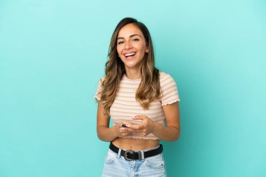 İzole edilmiş mavi arka planı olan genç bir kadın şaşırdı ve bir mesaj gönderiyor.