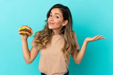 Soyutlanmış arka planda hamburgerini tutan genç bir kadın şüphe içinde el kaldırırken