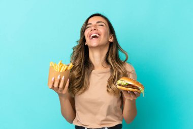 Arkaplanda kızarmış cips ve hamburger tutan genç bir kadın.