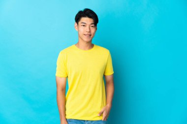 Genç Çinli adam mavi arka planda yalnız gülüyor.