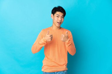 Mavi arka planda izole edilmiş genç bir Çinli baş parmak işareti yapıyor.