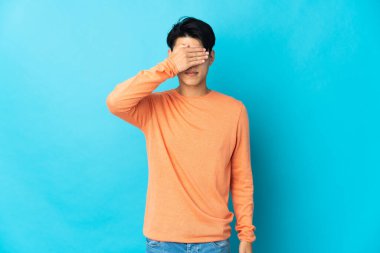 Genç Çinli bir adam mavi arka planda tek başına, gözleri elleriyle kapatıyor. Bir şey görmek istemiyorum.