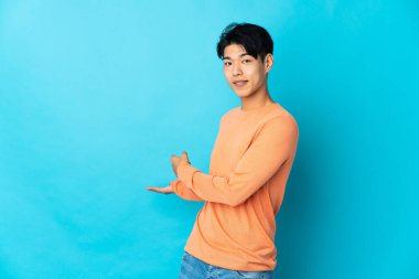 Mavi arka planda izole edilmiş genç bir Çinli davet etmek için ellerini yana uzatıyor.