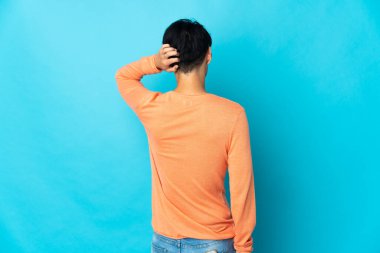 Genç Çinli adam arka planda mavi arka planda izole edilmiş ve düşünüyor