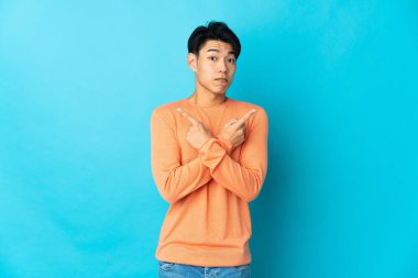 Mavi arka planda izole edilmiş genç Çinli adam, yandakilerin şüpheleri olduğunu gösteriyor.