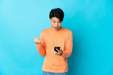 Mavi arka planda izole edilmiş genç bir Çinli şaşırmış ve bir mesaj göndermiş.