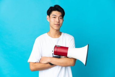 Mavi arka planda izole edilmiş genç bir Çinli elinde bir megafon ve gülümsüyor.