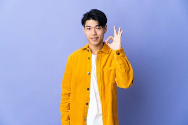 Mor arka planda izole edilmiş genç bir Çinli parmaklarıyla işaret veriyor.