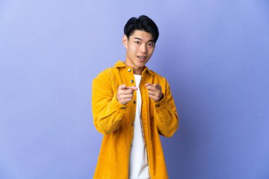 Mor arka planda izole edilmiş genç bir Çinli şaşırmış ve ön tarafı işaret ediyor.