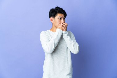 Genç Çinli bir adam mor arka planda izole edilmiş ağzını kapatıyor ve yan tarafa bakıyor.