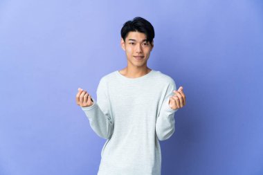 Mor arka planda izole genç Çinli adam para hareketi yapıyor.