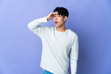 Mor arka planda izole edilmiş genç bir Çinli yan tarafa bakarken sürpriz jest yapıyor.