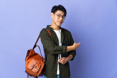 Young student woman isolated on purple background pointing back